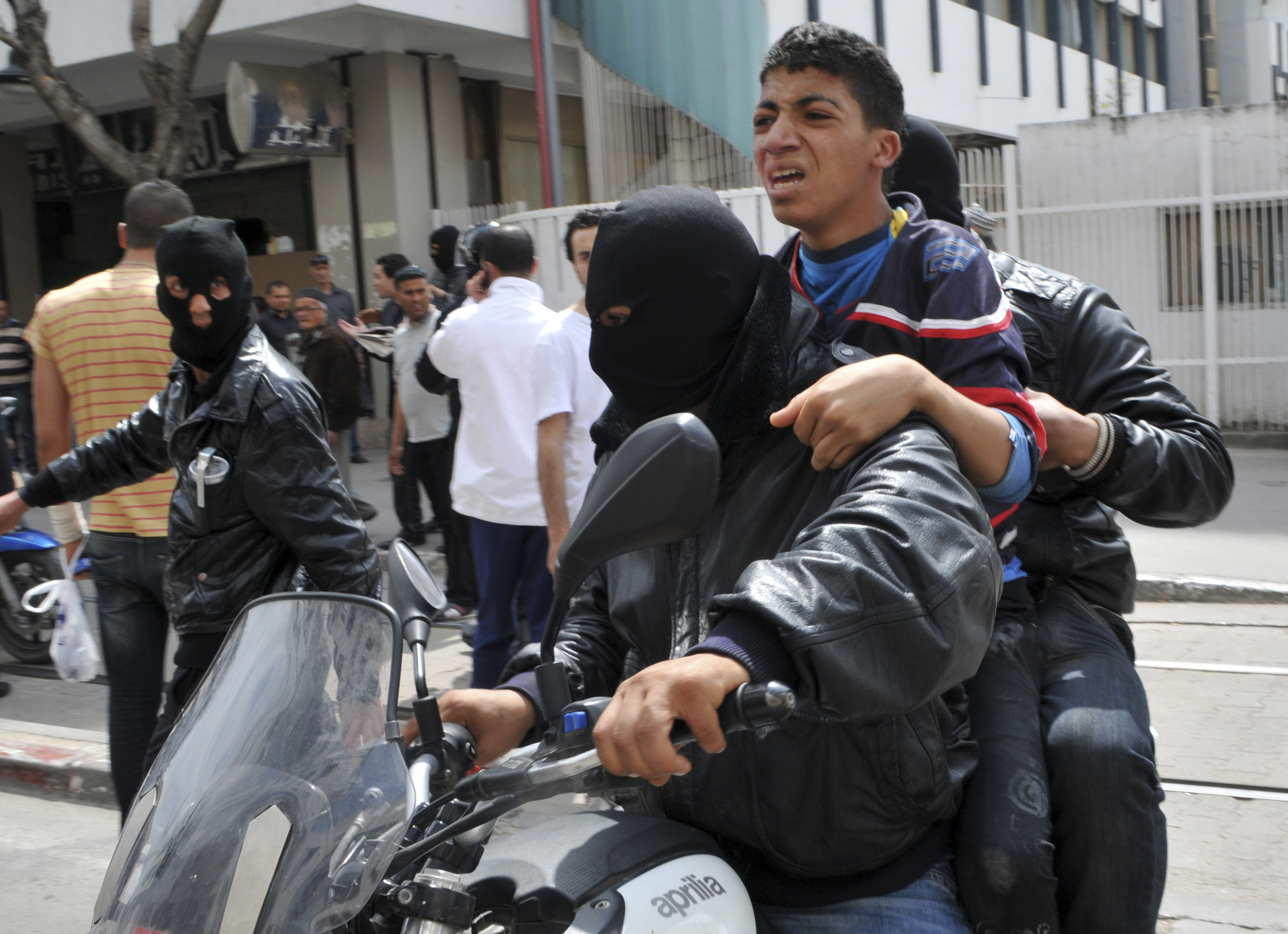 En ung man förs bort av maskerade poliser under upploppen i Tunisien.