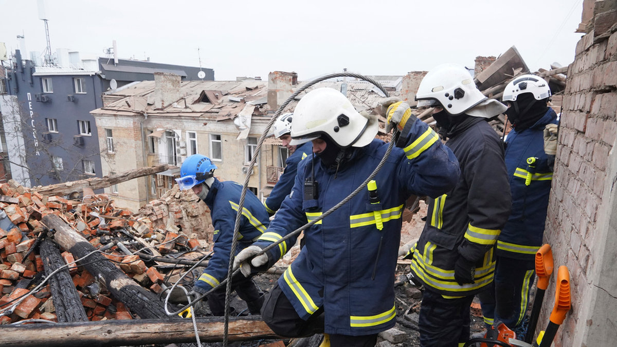 Ukrainska räddningsarbetare röjer på taket av en byggnad som träffats i en rysk robotattack mot staden Charkiv.