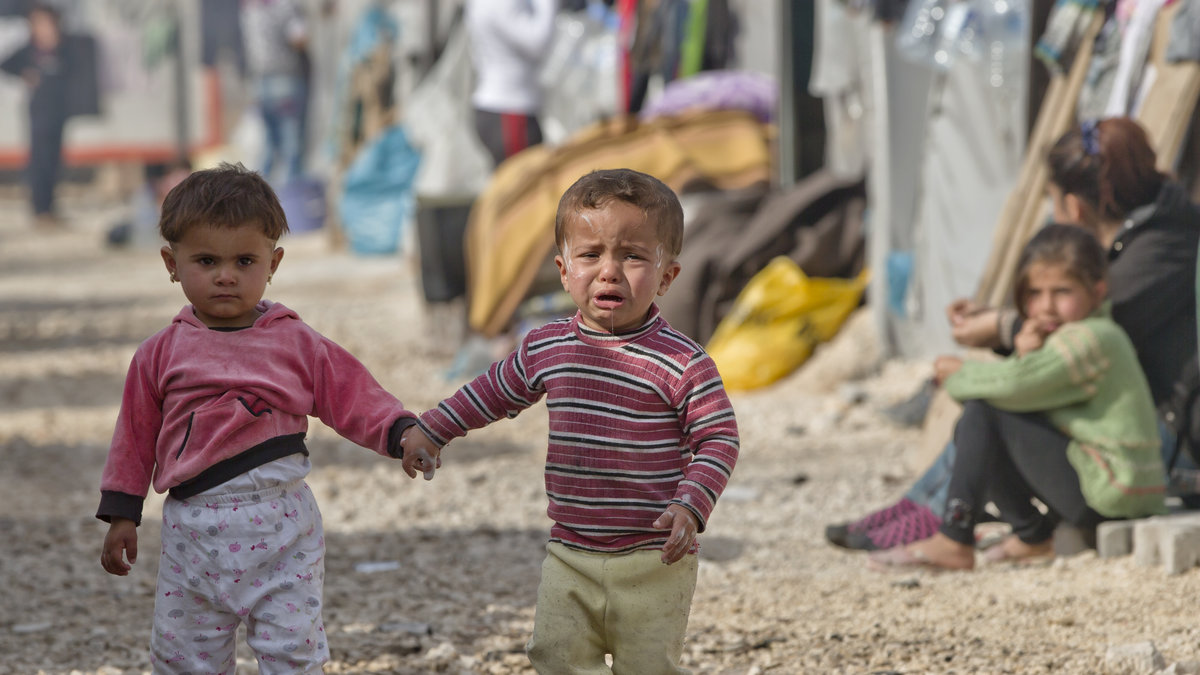 Två flyktingbarn håller handen på en flyktingförläggning vid den syriska gränsen. 
