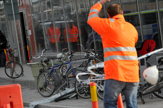 En glasruta från en kontorsfastighet o centrala Stockholm lossnade i vindbyarna och det var ren tur att ingen skadades. På bilden syns hur en en fastighetsskötare får hjälmen avblåst då han spärrar av området. 