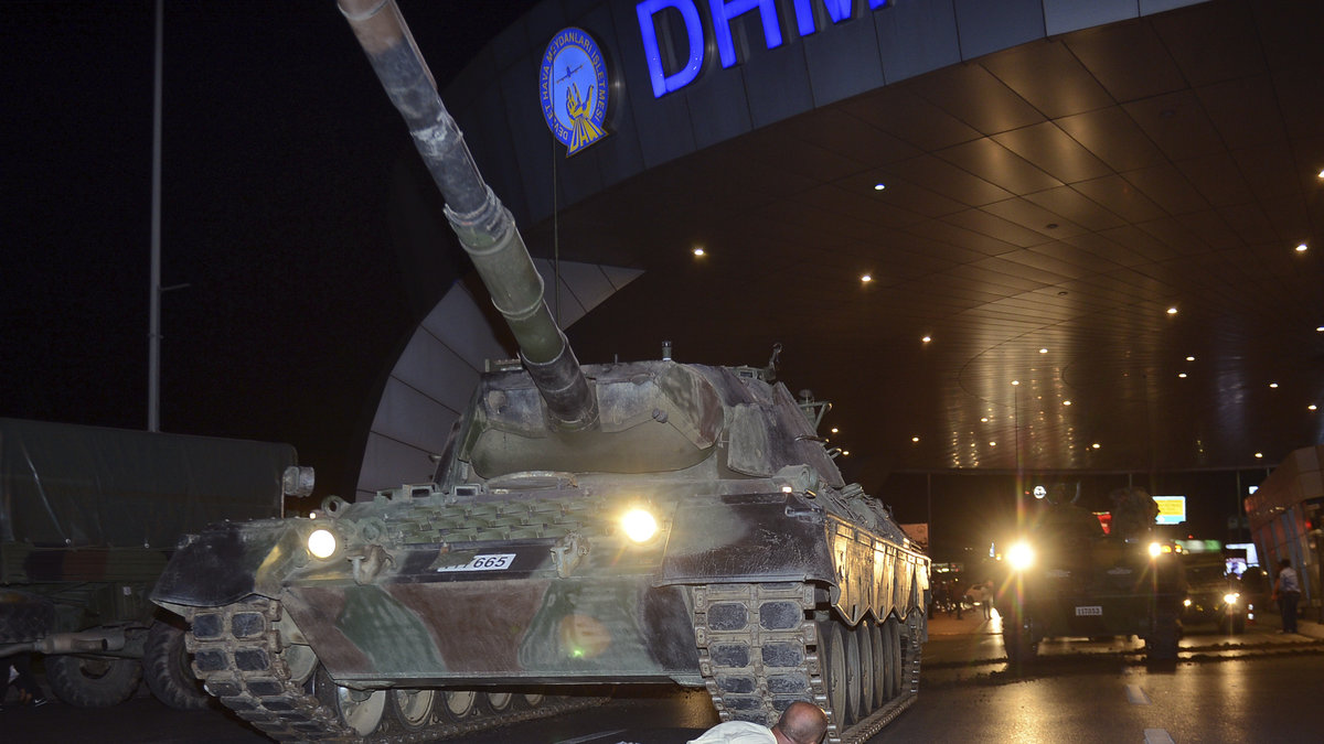 En man gömmer sig bakom en pansarvagn vid flygplatsen i Istanbul.