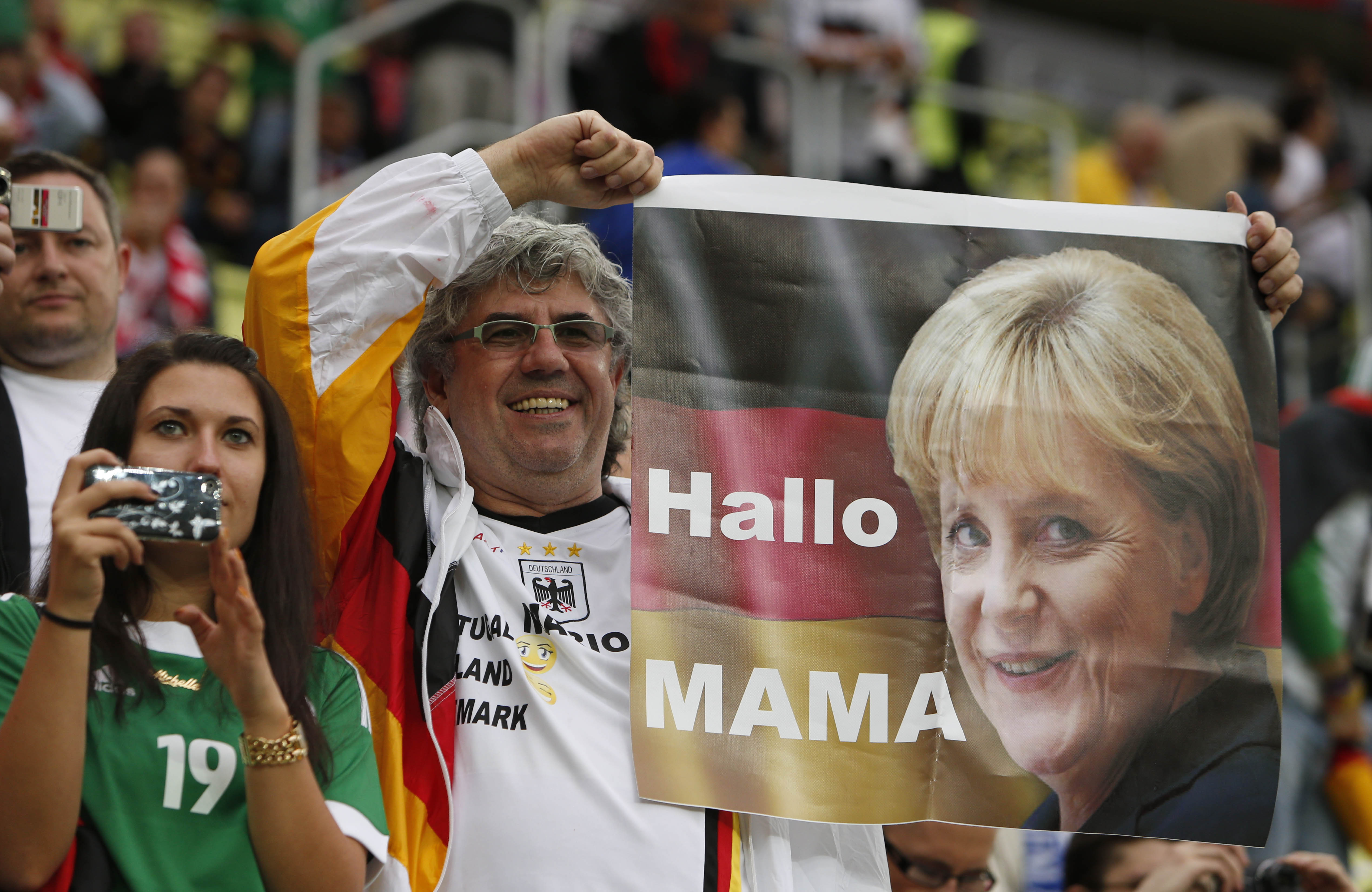 Medan ett tyskt fans hånar de grekiska fansen med sin "landsmoder" Angela Merkel. Medan ett tyskt fans hånar de grekiska fansen med sin "landsmoder" Angela Merkel.