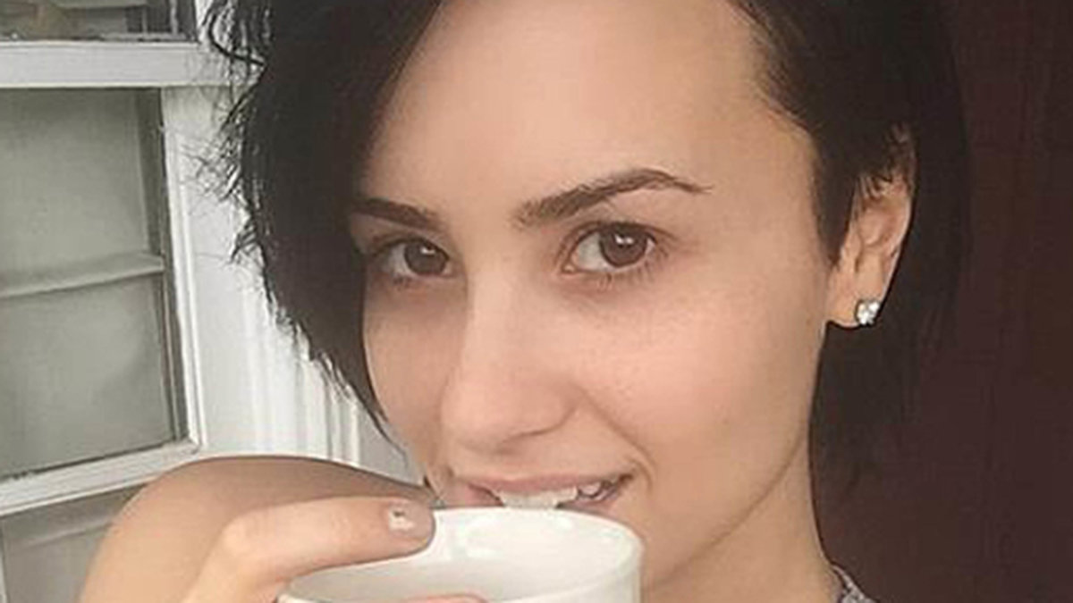 En osminkad Demi Lovato tar en kopp kaffe. 