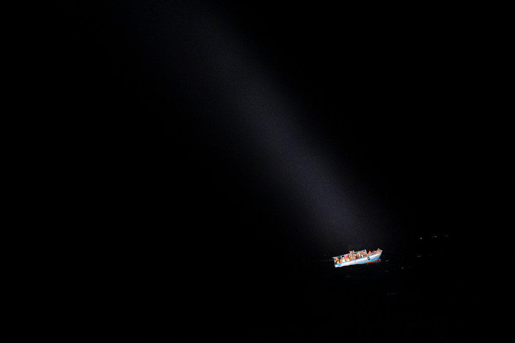 En strålkastare lyser på en båt med migranter. Denna befann sig i Medelhavet under tisdagen. Arkivbild.
