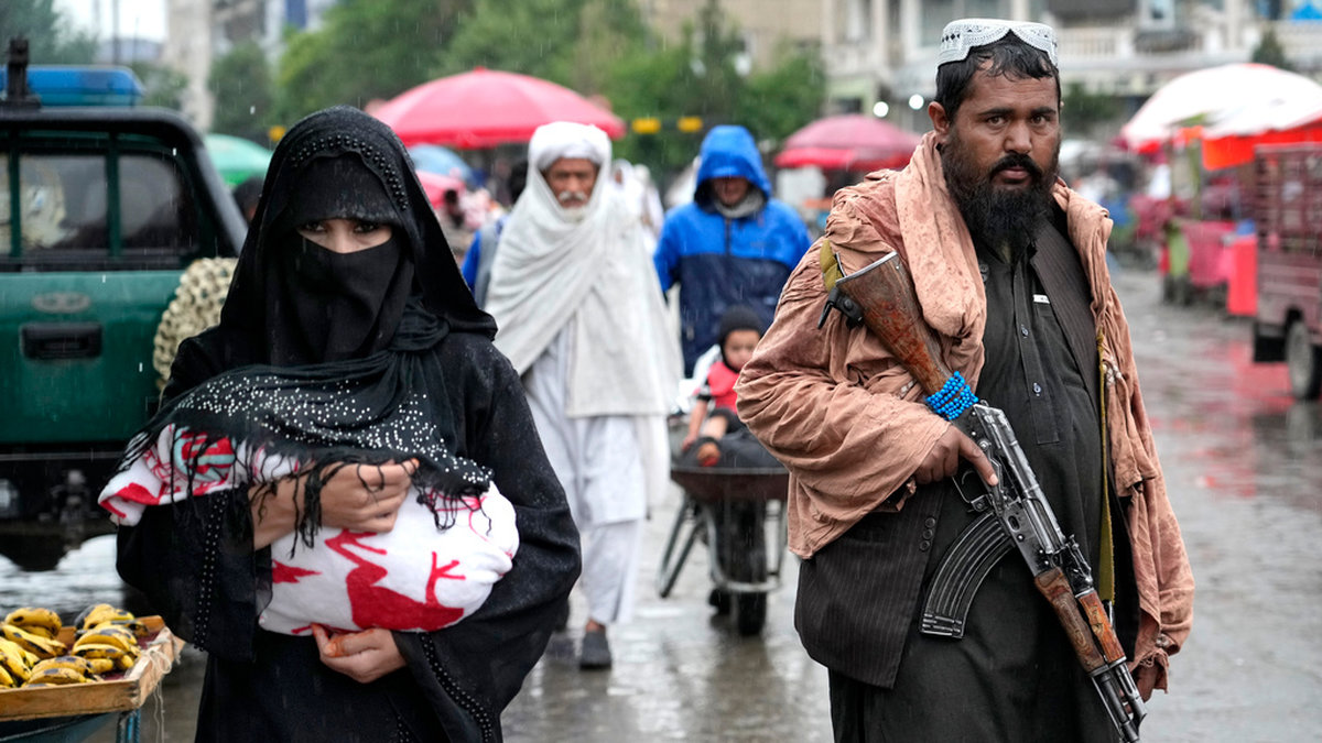 En afghansk kvinna går genom en marknad i Afghanistans huvudstad Kabul och en talibankrigare håller vakt. Arkivbild.