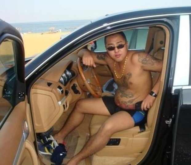 Glider runt i en lyxig bil med solglasögon, bar överkropp och tatueringar. 