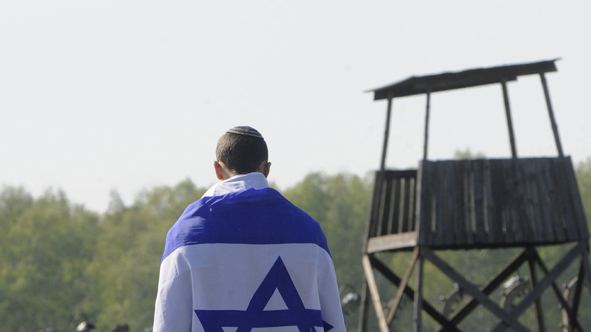 En man går tillsammans med den israeliska flaggan på spåret som ledde judarna in i Auschwitz.