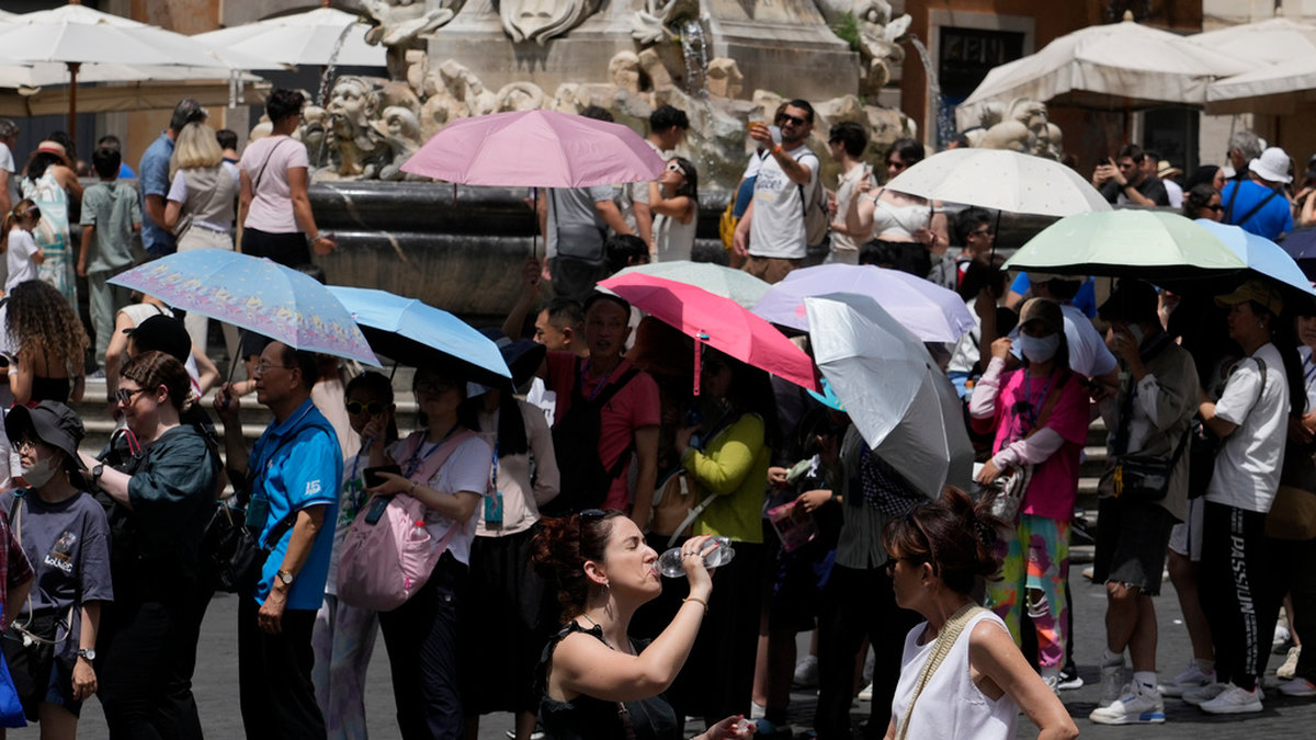 Turister använder paraplyn för att skydda sig mot solen när de köar till Pantheon i Rom under sommarens värmebölja. Bild från juli.