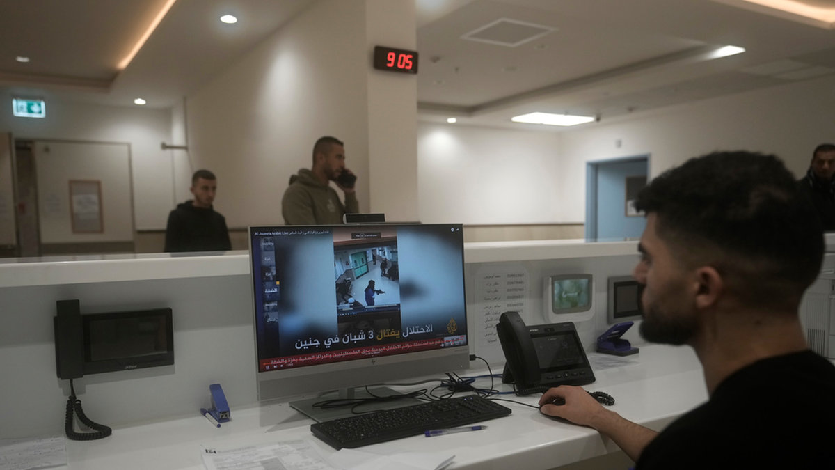 En anställd på Ibn Sina-sjukhuset tittar på ett nyhetsinslag om den israeliska räden.