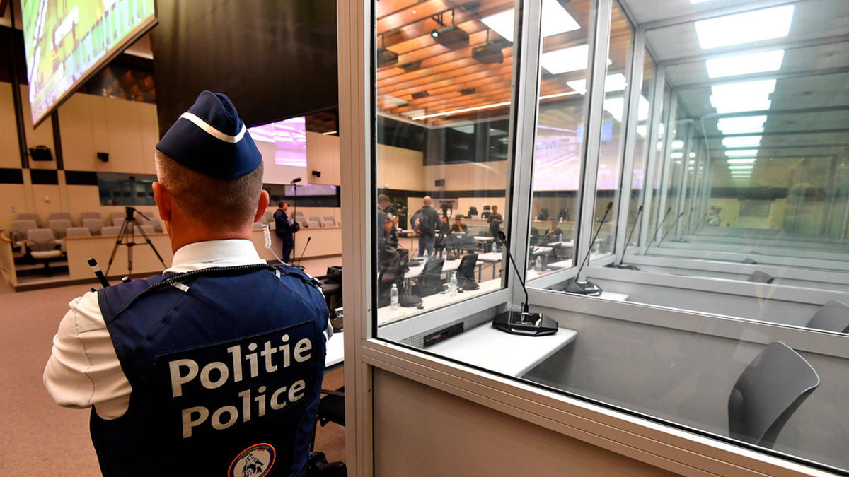 En polisman står invid de glasburar för anklagade i terrorrättegången i Bryssel. Glasburarna byts efter klagomål från försvaret ut och nu har rättegångsstarten försenats flera veckor. Arkivbild.
