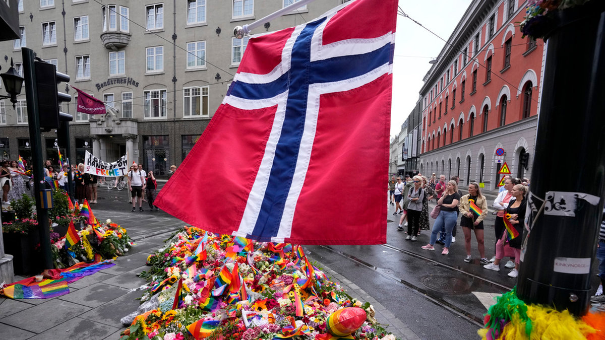 En norsk flagga ovanför blommor och regnbågsflaggor som placerats vid brottsplatsen i centrala Oslo.