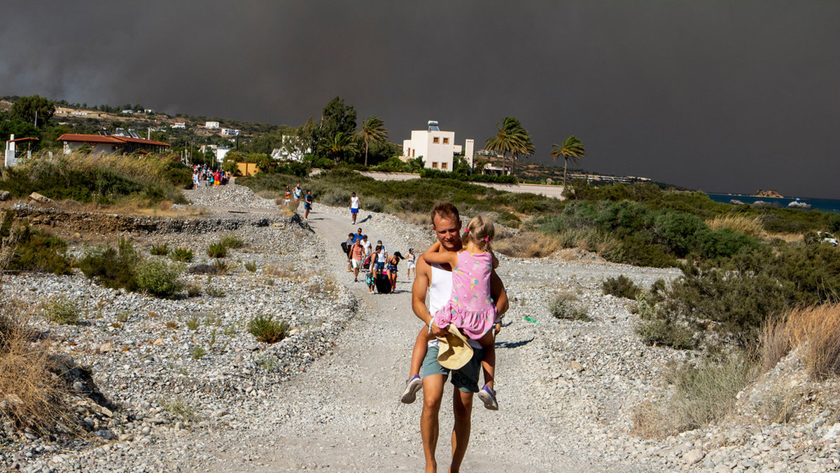 En turist bär sitt barn bort från ett brandområde på den grekiska semesterön Rhodos under lördagen.