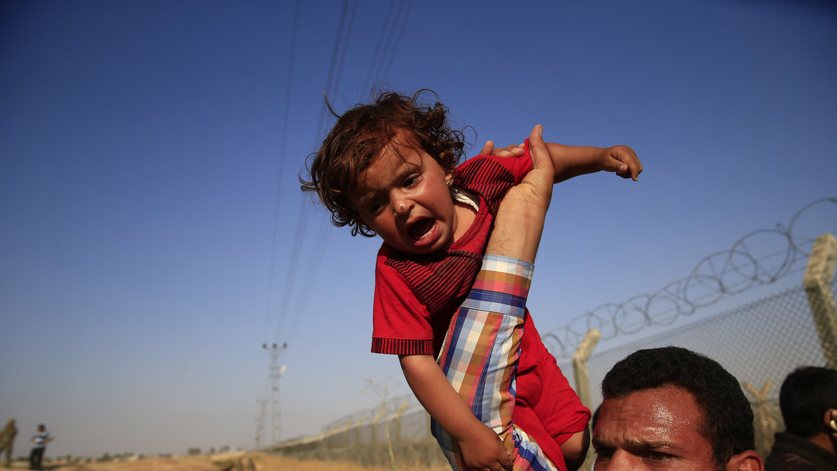 En syrisk flyktnin som bär sitt barn över ett trasigt stängsel som är mellan Syrien och Turkiet. 