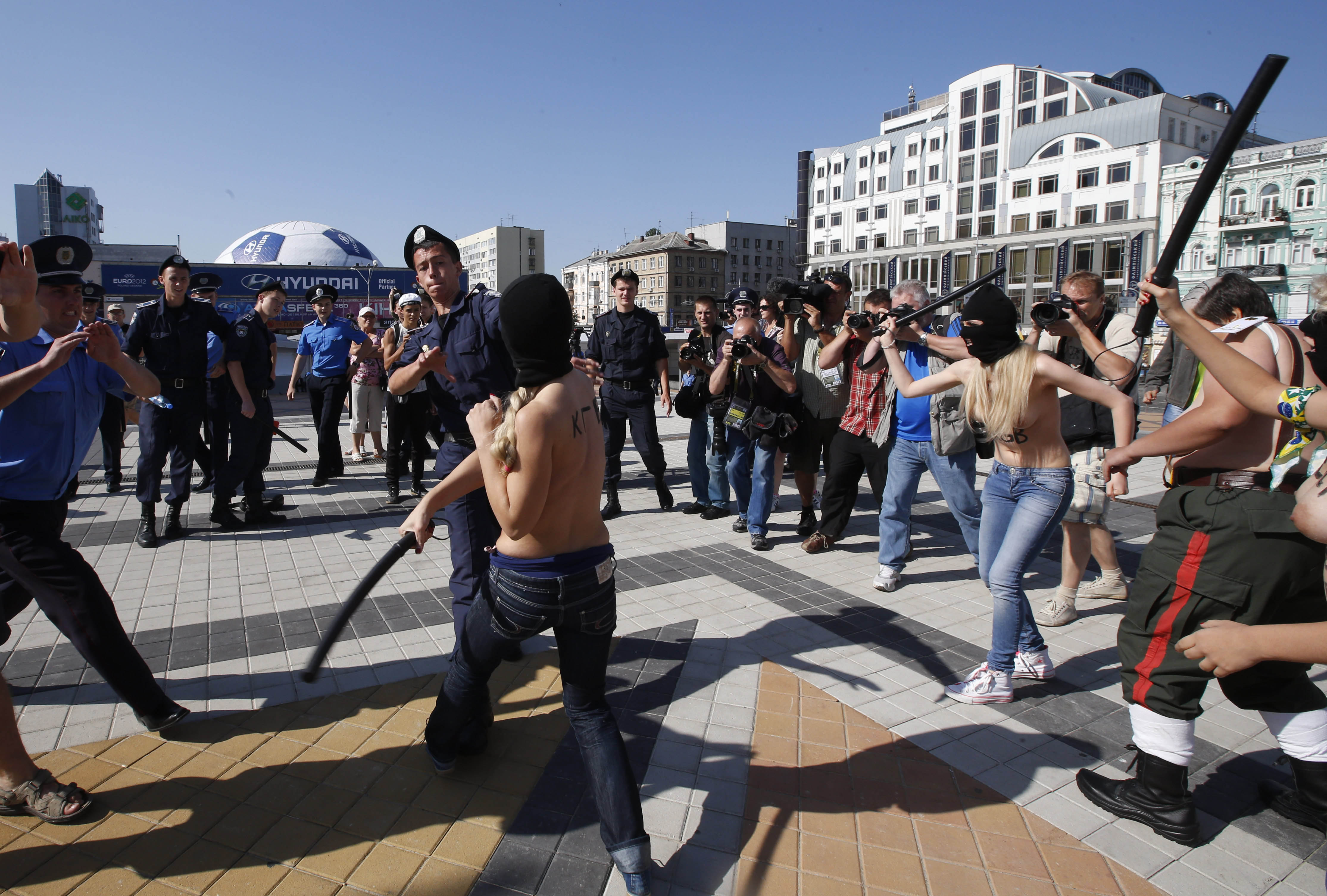 På sedvanligt vis protesterar gruppen utan tröjor. De använder gummiklubbor mot den ukrainska polisen.