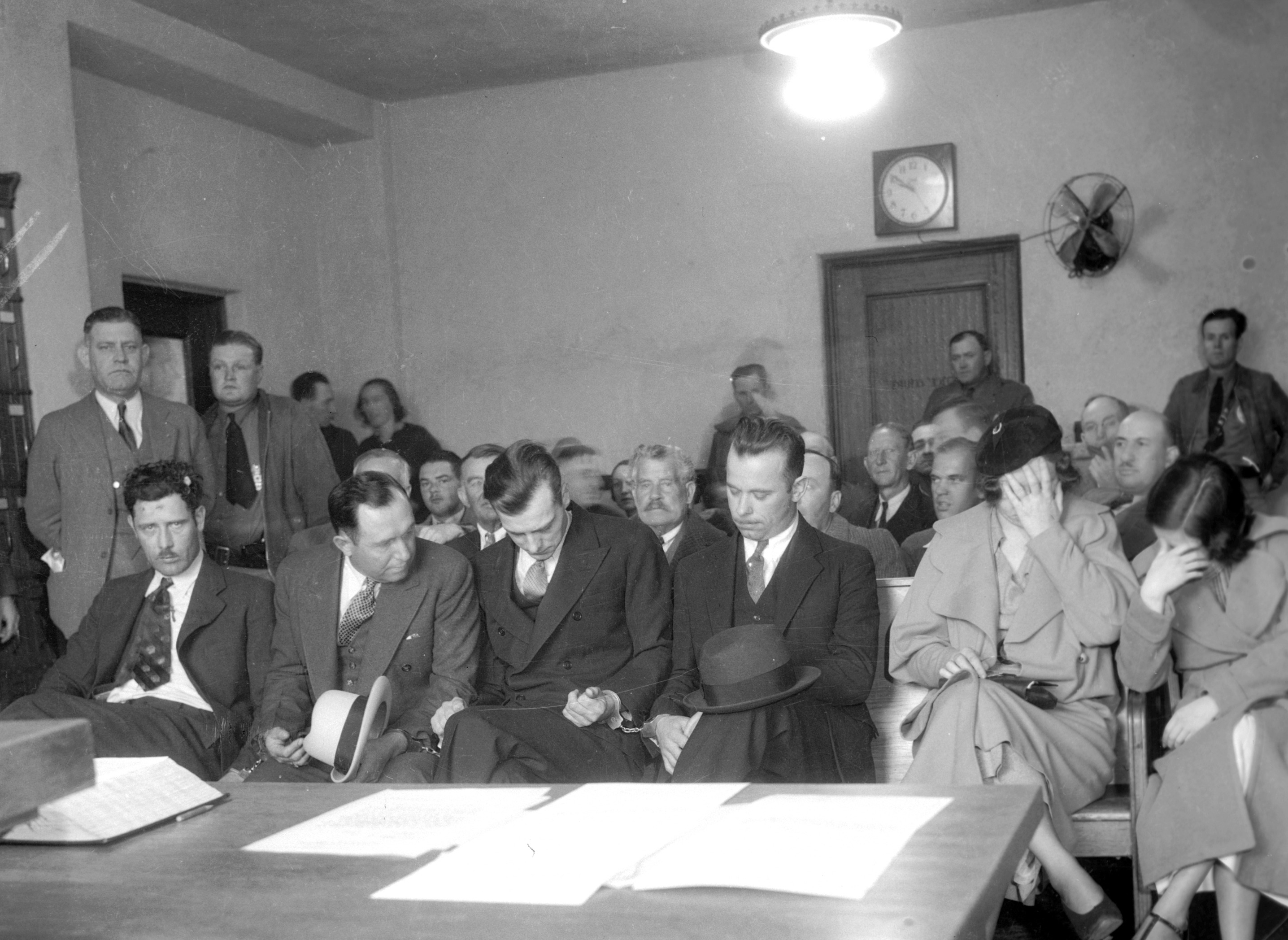 Här syns John Dillinger med sitt maffiagäng. Från vänster sittandes: Russel Clark, Charles Makley, Harry Pierpont, John Dilliger. Vid en rättegång från 1934.