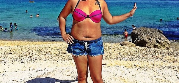 Kvinna står på standen i rosa bikini och jeansshorts Bada är inte helt fel
