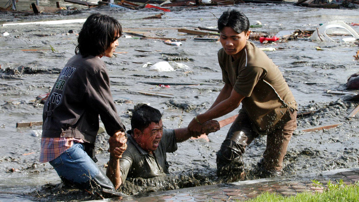 Två ungdomar kämpar för att få upp en man ut vattnet på en gata i Banda Aceh, Indonesien, ett av de värst drabbade ställena.