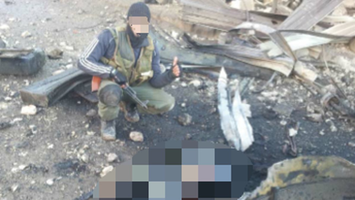 En okänd IS-krigare poserar med en sönderbränd kropp. På grund av att bilden är extremt obehaglig har Nyheter24 valt att censurera kroppen. 